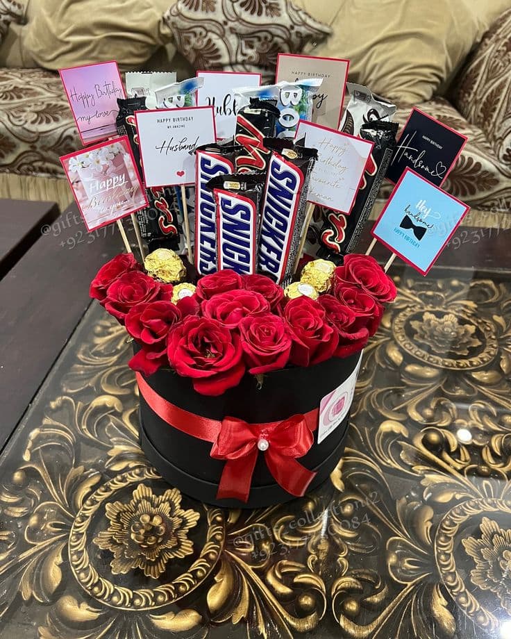 Black gift box filled with red roses, Snickers bars, chocolates, and birthday greeting cards.