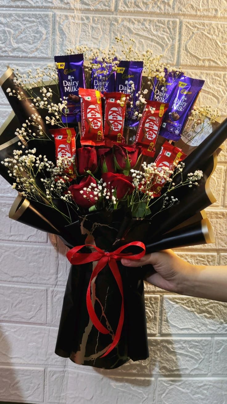 Hand holding a bouquet of red roses, baby's breath, KitKat, and Dairy Milk chocolates.