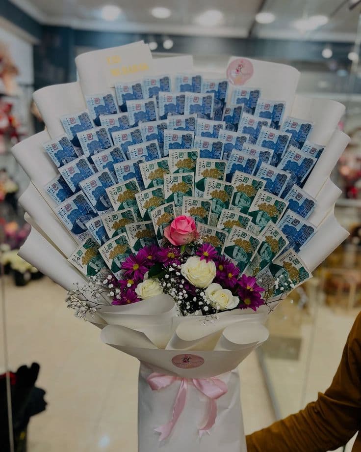 Large bouquet of Pakistani Rupee banknotes and fresh flowers wrapped in white with pink ribbon.