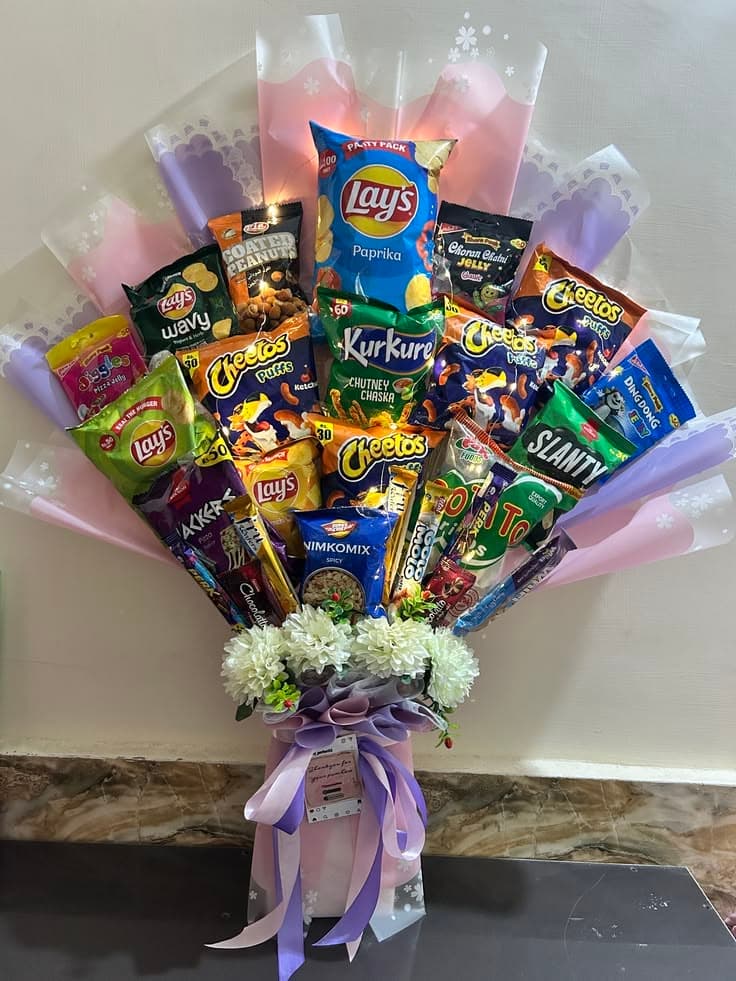 Snack bouquet with chips, candies, and fairy lights, wrapped in pink paper with white flowers.