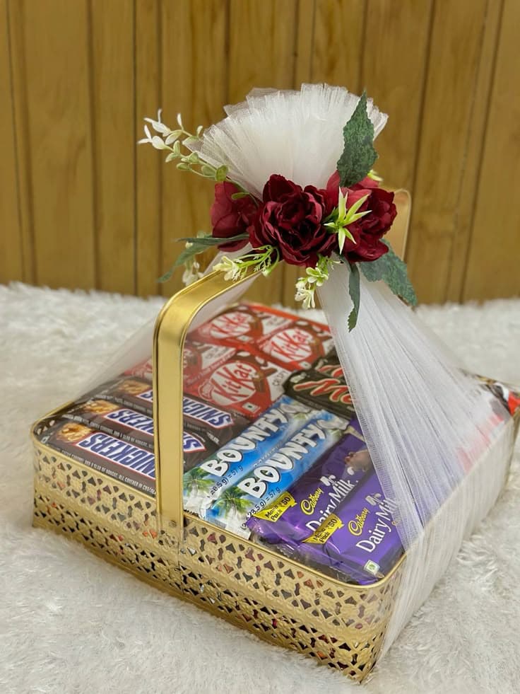 Gold gift basket filled with assorted chocolates, wrapped in white tulle with red flowers.