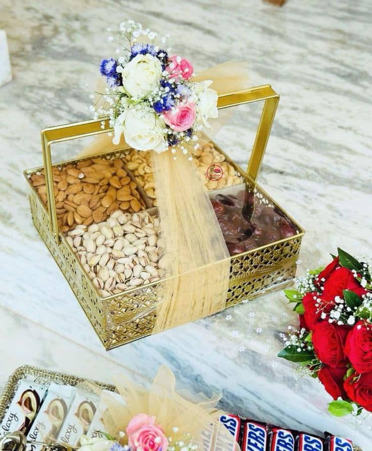 Gold gift basket with almonds, cashews, pistachios, and dates, decorated with roses and gold tulle.